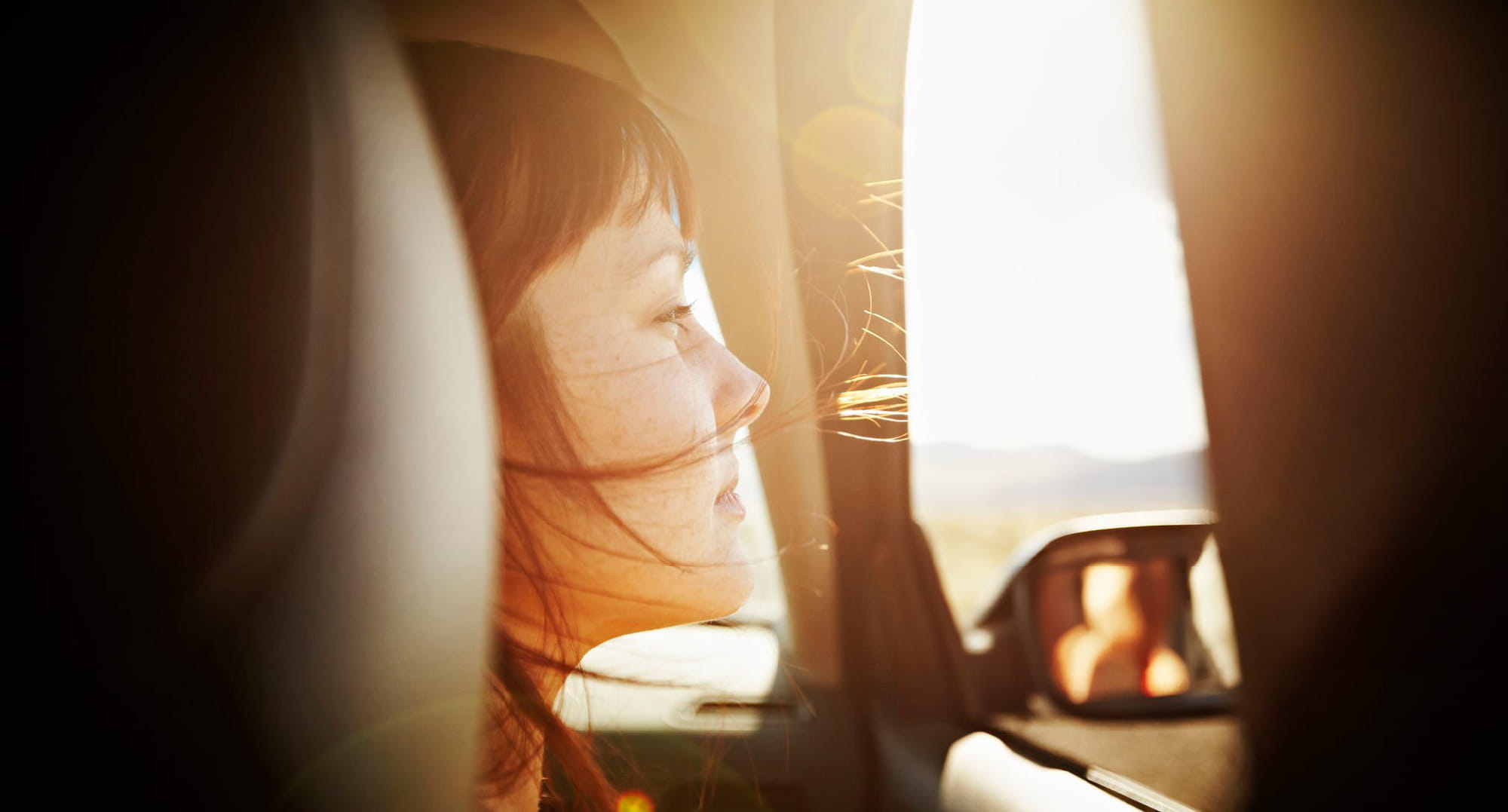 車窓から笑顔で外を眺める女性のイメージ。