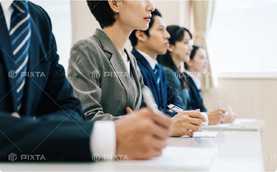 研修会や会議で真剣な表情で話を聞くスーツ姿の社員たちのイメージ画像