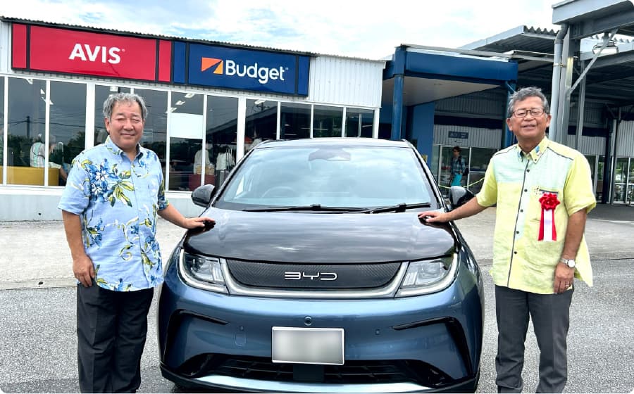 電気自動車（EV）に手を添えて微笑む、二人の男性の写真