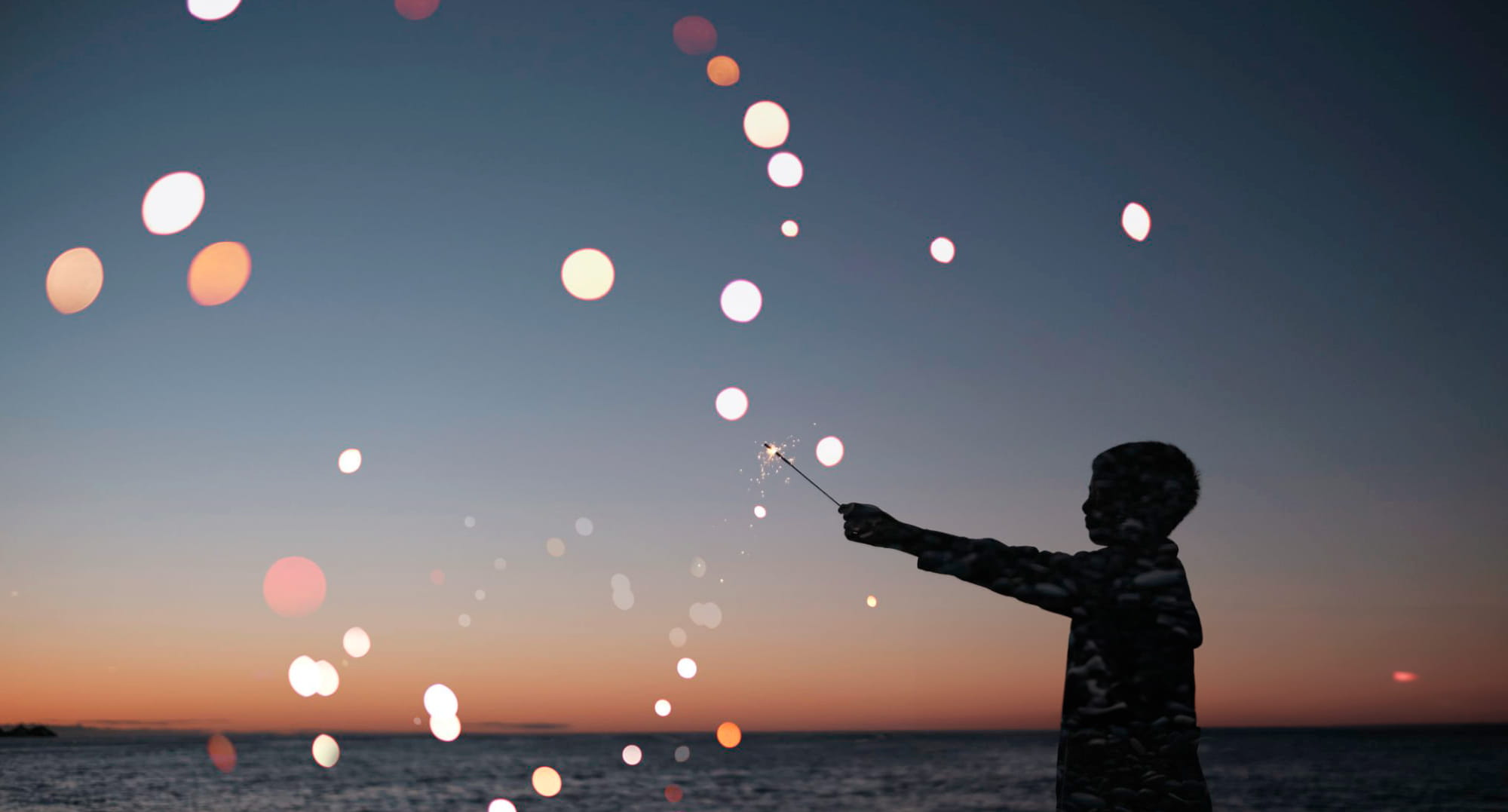 夕暮れの中、手持ち花火の光を見つめる子供のシルエットのイメージ