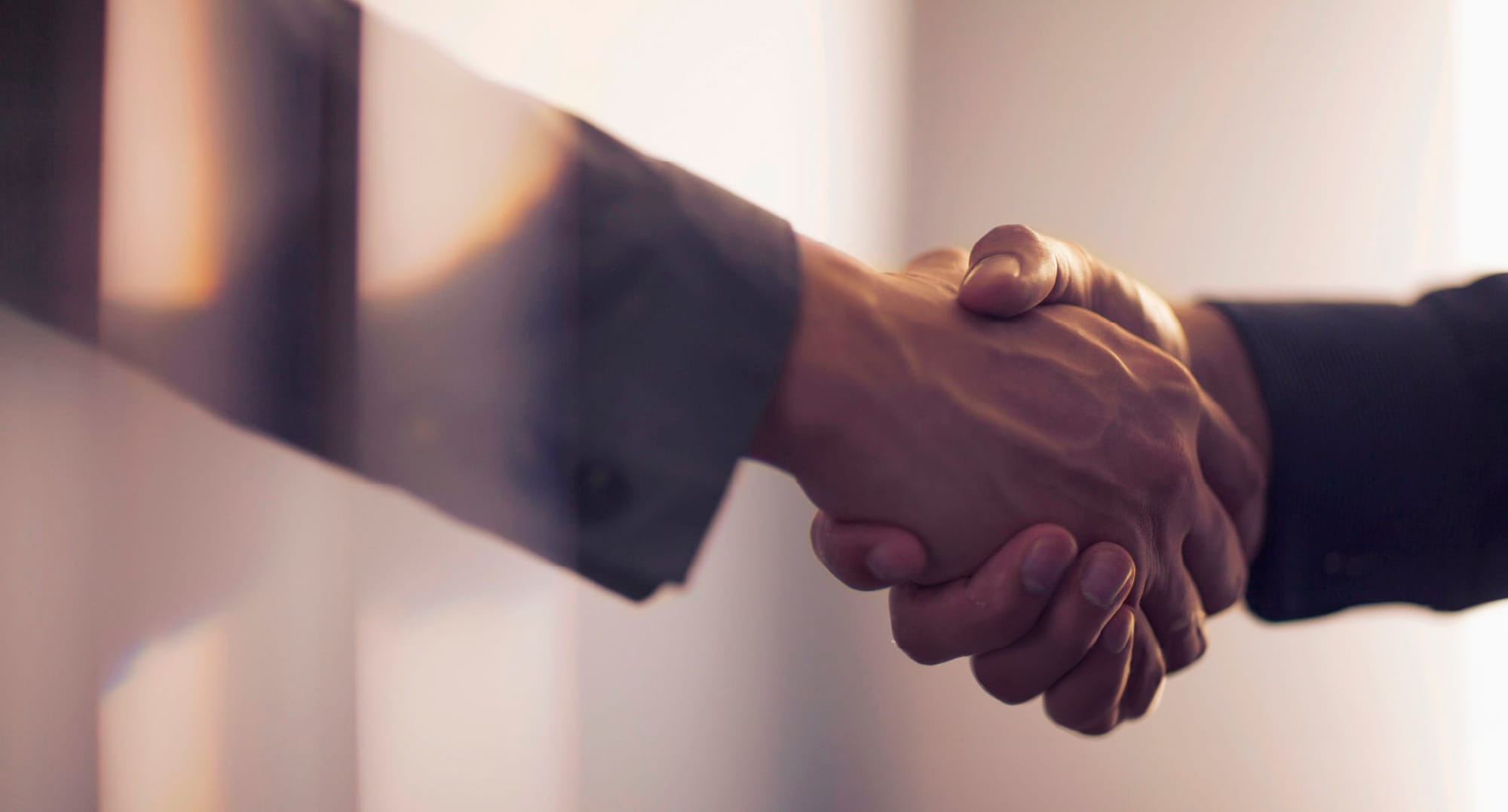 スーツ姿の男性同士の、握手する手にフォーカスしたイメージ。