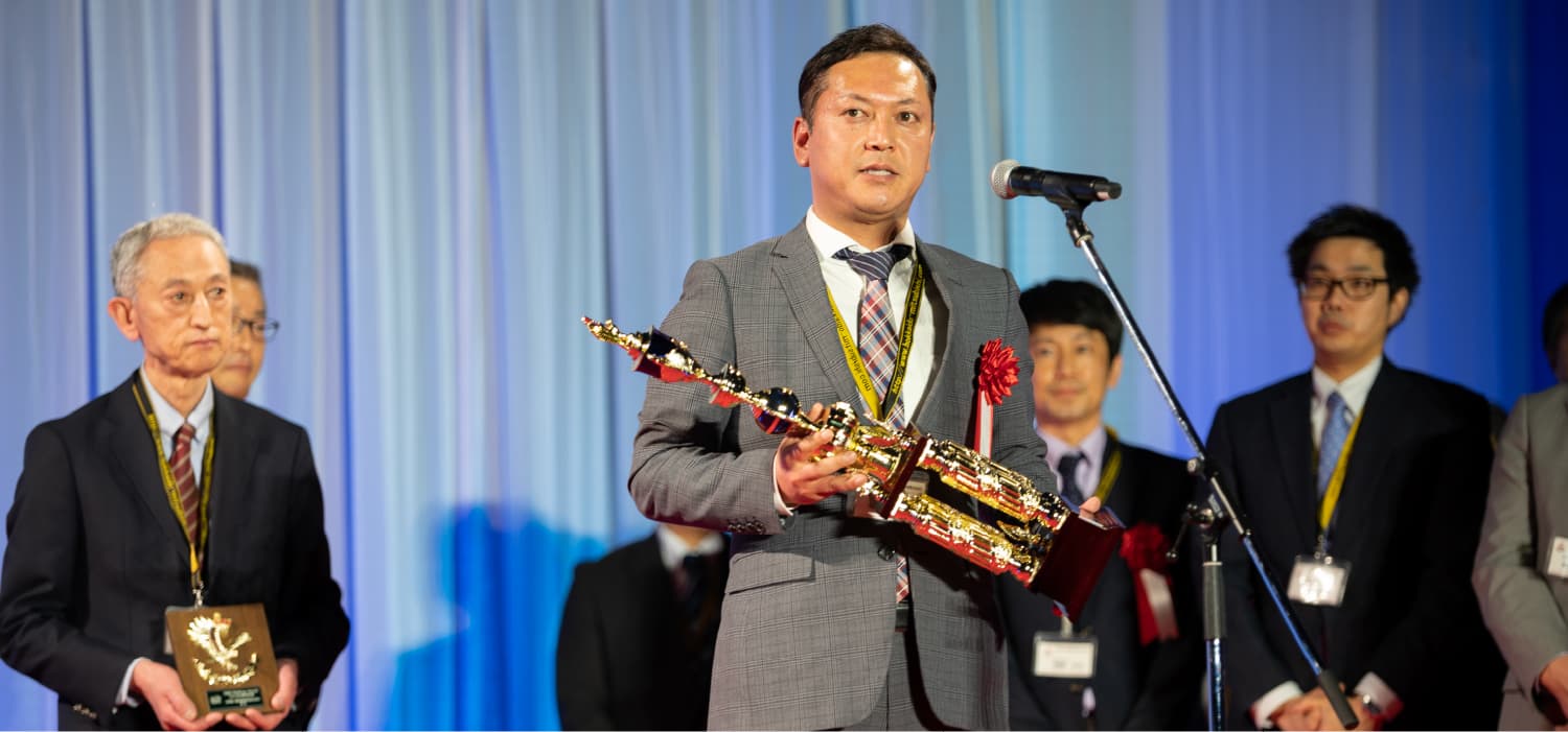 トロフィーを抱えスピーチをするスーツ姿の男性のイメージ