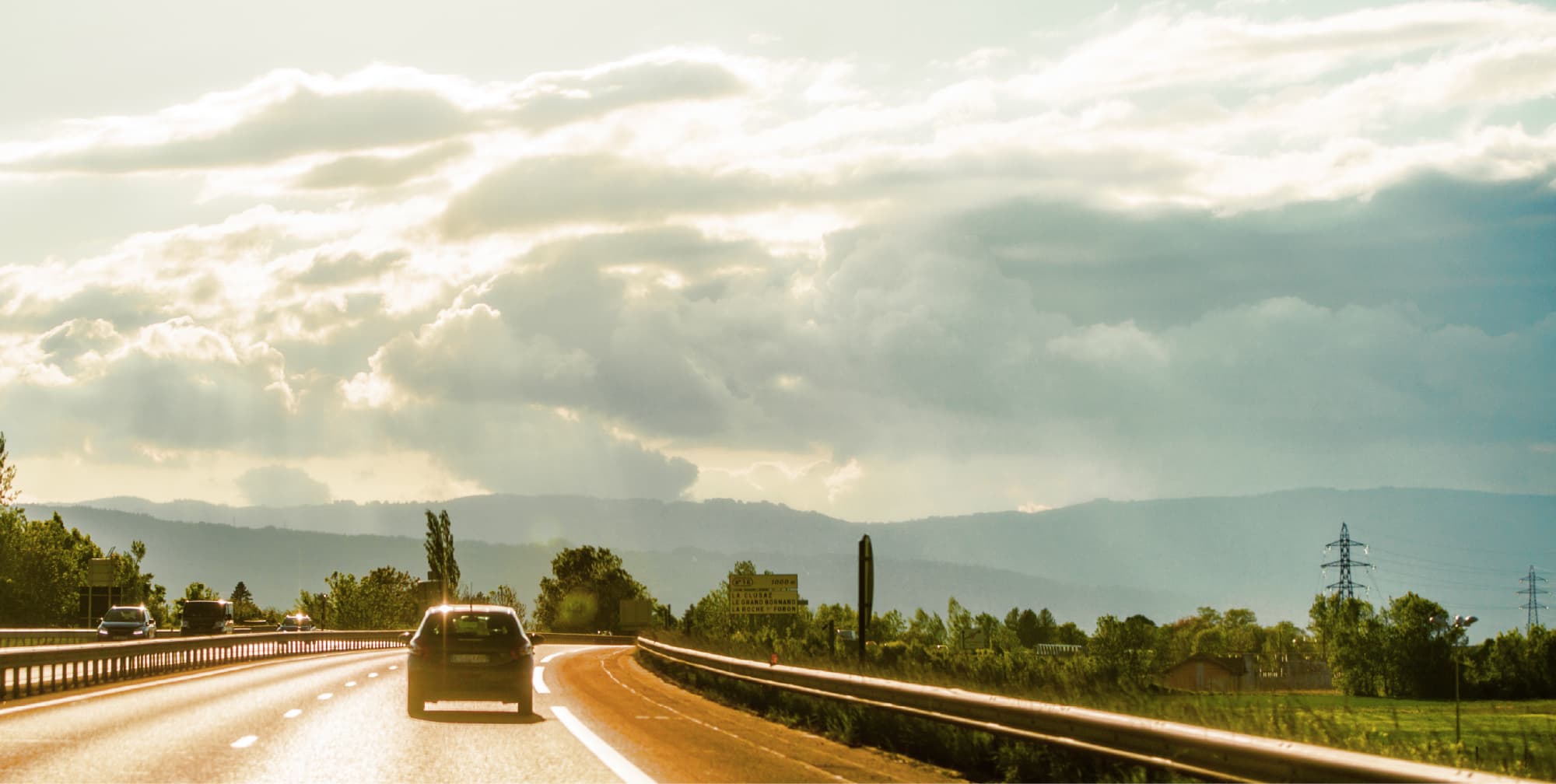 山並みと空が広がる風景の中を走る道路と自動車のイメージ